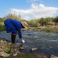 Person bending down in stream to collect water 