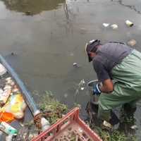 Person bending down next to river litter boom with a bucket