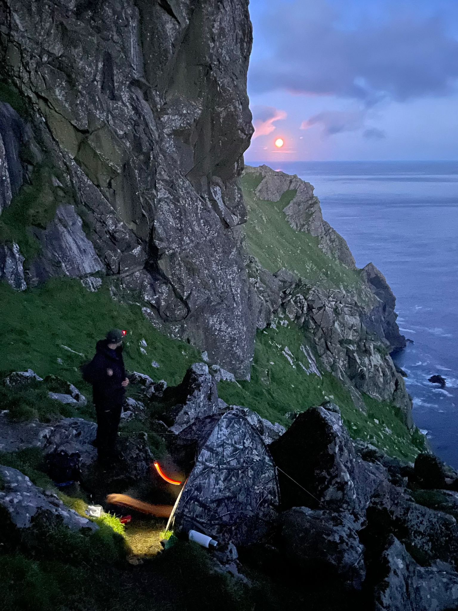 Photograph of a fieldworker on a cliffside St Kilda at sunset (image courtesy of Brennig Hughes)